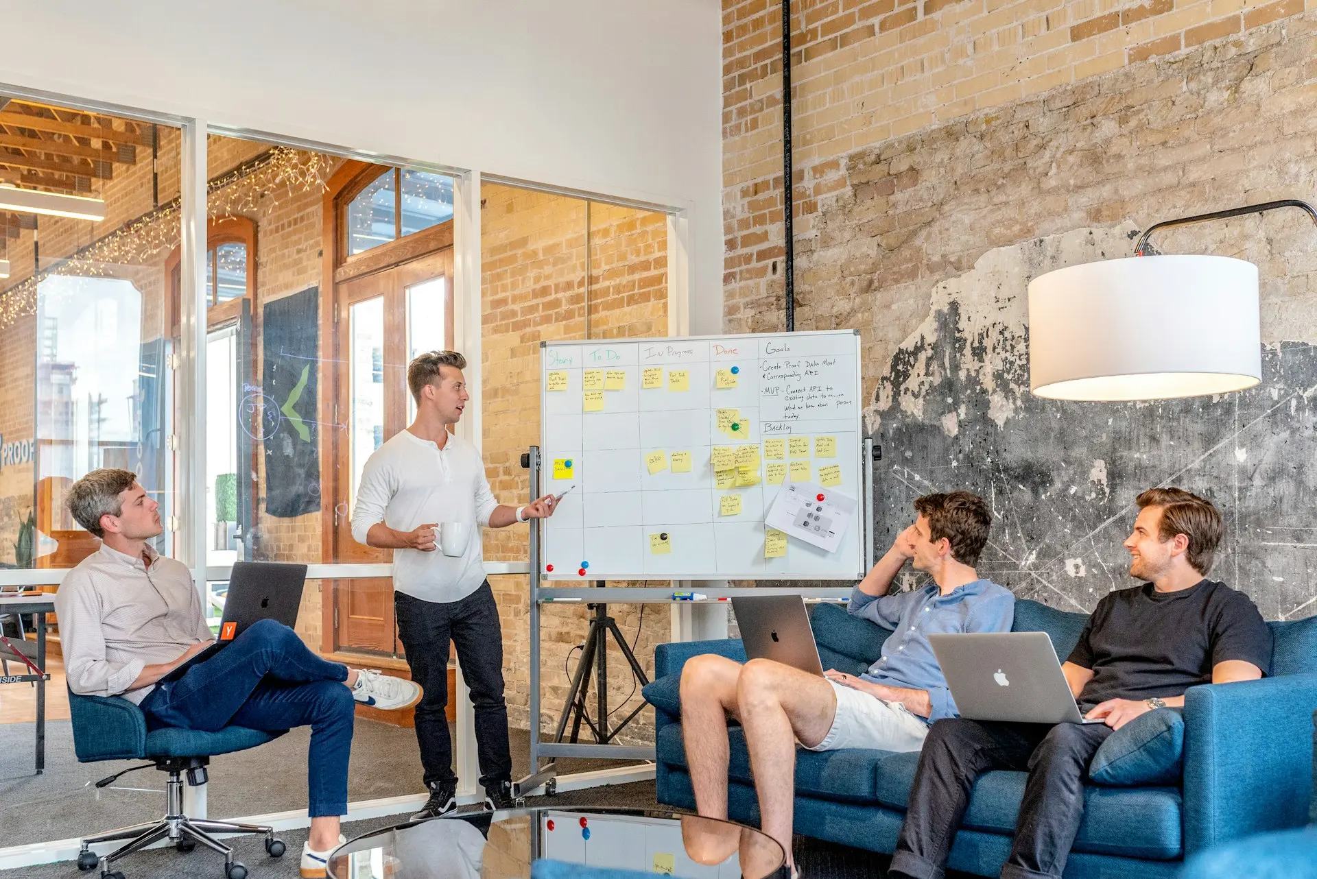 three men sitting while using laptops and watching man beside whiteboard